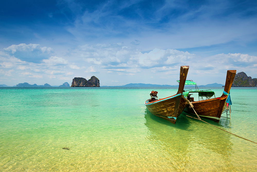 Two wooden longtail boats mooring on the beach with limestone rock formation in the background (Photo by Sunphol Sorakul / Getty Images)